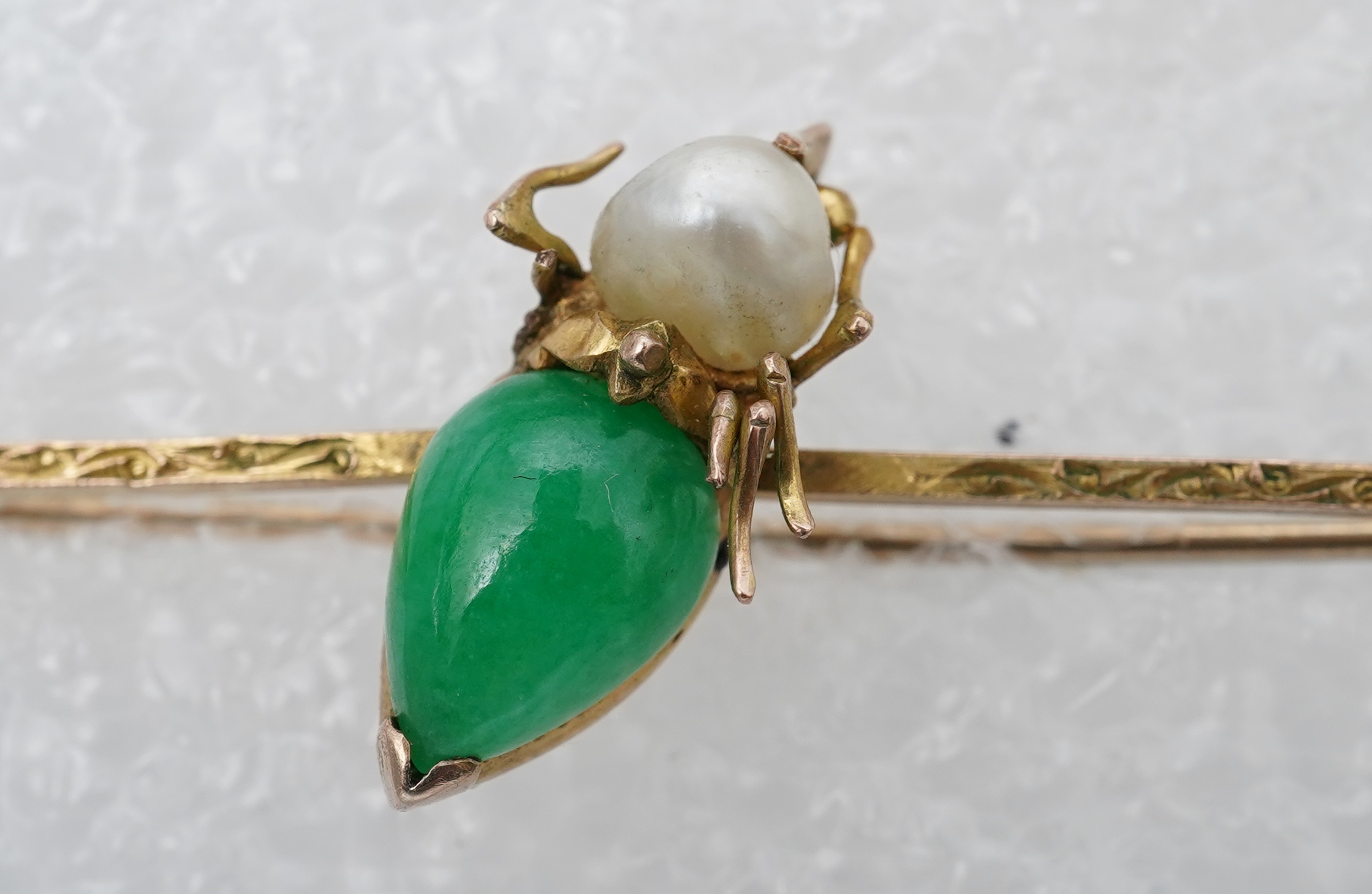 Two stick pins and a jadeite bar brooch, comprising: a bar brooch centring on an insect set with a pear-shape jadeite cabochon and a pearl, mounted in gold, length 7.5cm, stamped 14K, base metal pin; a stick pin capped w